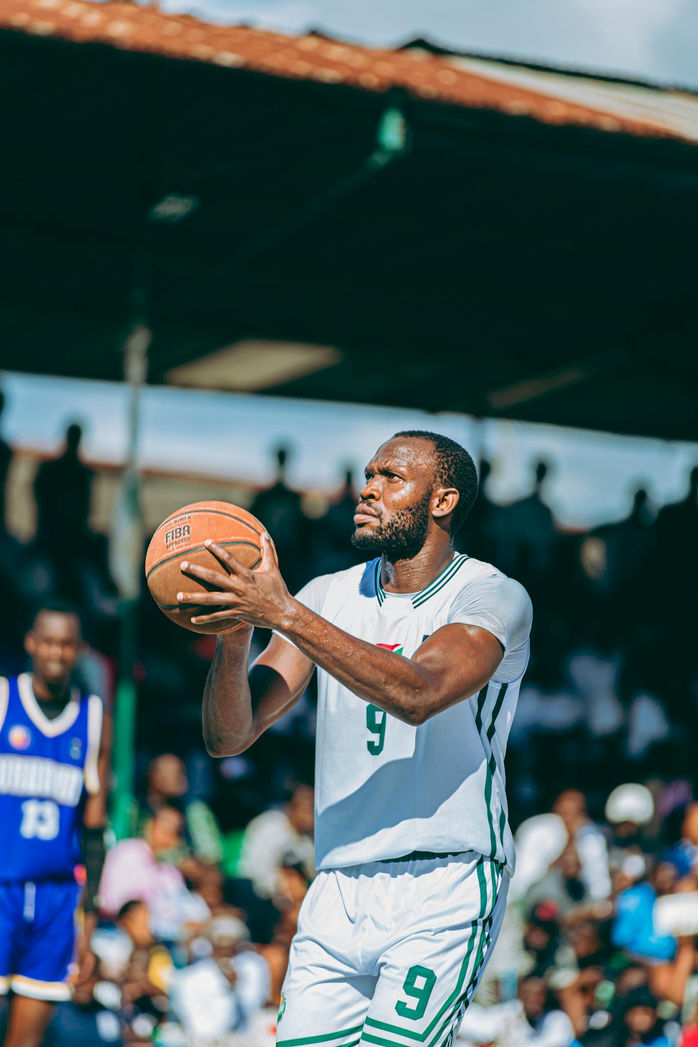 A basketball player focuses intently as he prepares to shoot during an outdoor game on a sunny day.