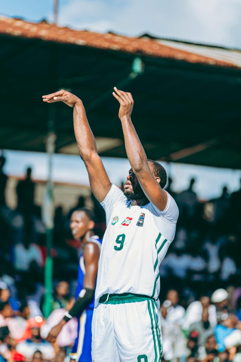 A basketball player makes a jump shot during an outdoor match, crowd watching.
