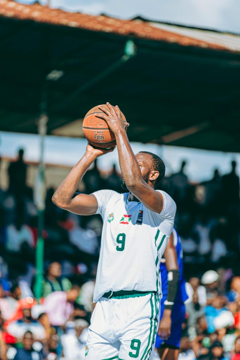 Focused basketball player shooting a hoop during an intense outdoor game, surrounded by a lively crowd.