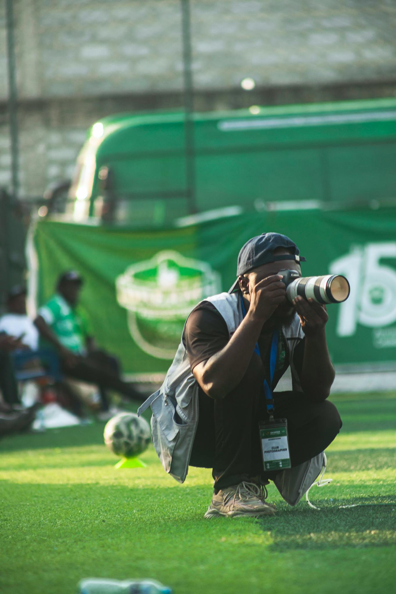 Photographer kneeling on grass field capturing a football game with professional camera.
